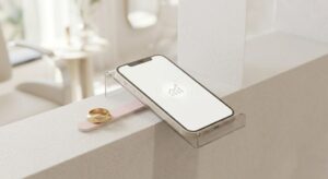 A Mobile Phone Sitting On A Modern Clear Acrylic Display Stand Showing A Minimalist Business Growth Icon Inside A Brightly Lit Beauty Studio.