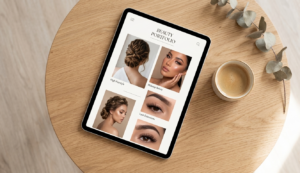 A Top-Down Perspective Of A Modern Silver Tablet Resting On A Light Oak Wood Table In Soft, Natural Daylight. The Tablet Screen Displays A Polished, Minimalist Digital Portfolio Layout For A Beauty Professional, Showcasing High-Quality Portraits Of Hairstyling And Makeup Artistry. A Small Ceramic Coffee Cup And A Sprig Of Dried Eucalyptus Are Nearby. The Composition Is Focused And Organized, Embodying A Sophisticated Approach To Displaying A Professional Portfolio Via Digital Salon Management Tools.
