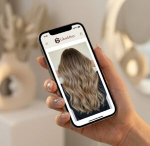 A Manicured Hand Holds A Smartphone, Displaying A Sharp Photograph Of A Complex Hair Transformation. The Mobile App Interface Surrounding The Image Is Clearly Branded For The Glowhives Platform, Featuring The Corrected &Quot;Glowhives&Quot; Text Above The Transformation Photo.